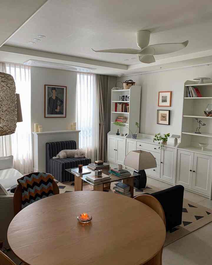 ナチュラルな色調のリビング、木製の円形テーブルと白い本棚、照明、犬がいる温かみのある雰囲気のインテリア