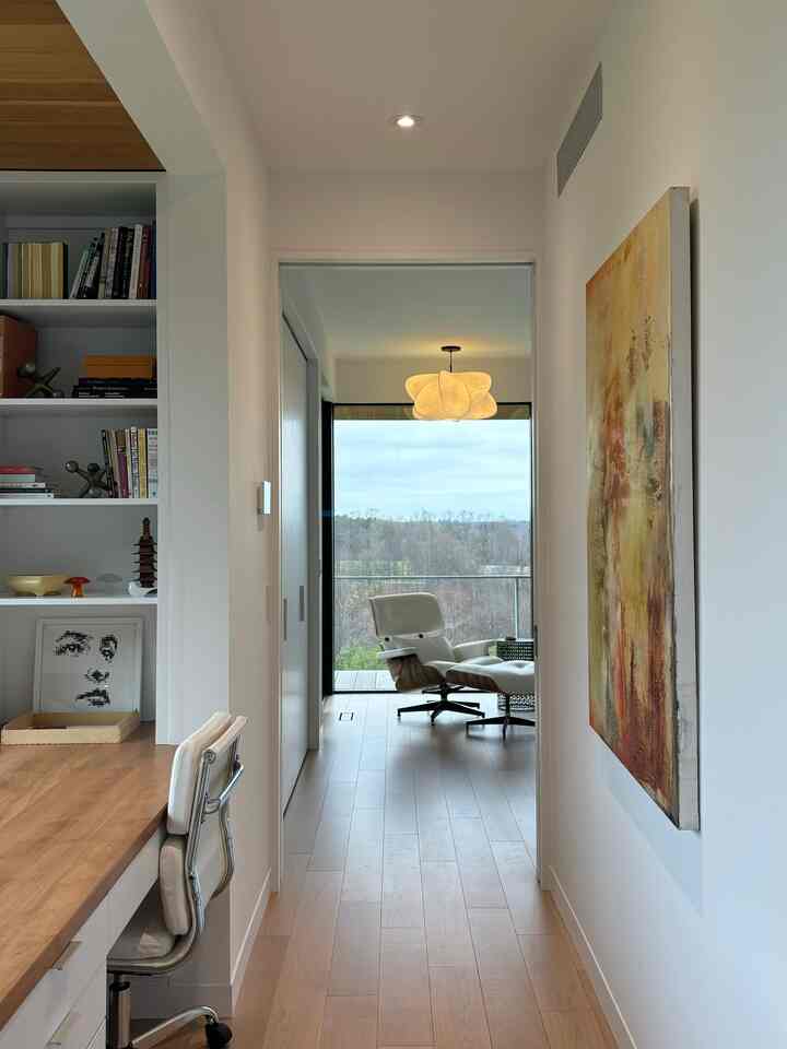 Modern narrow hallway and home office area with white and wood tones, featuring a balcony and iconic Eames Lounge Chair