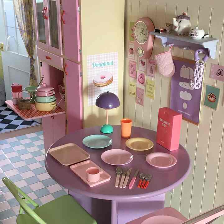 Kitchen and dining room with pink and purple tones, featuring a round table set with various plates and cutlery in a cozy atmosphere