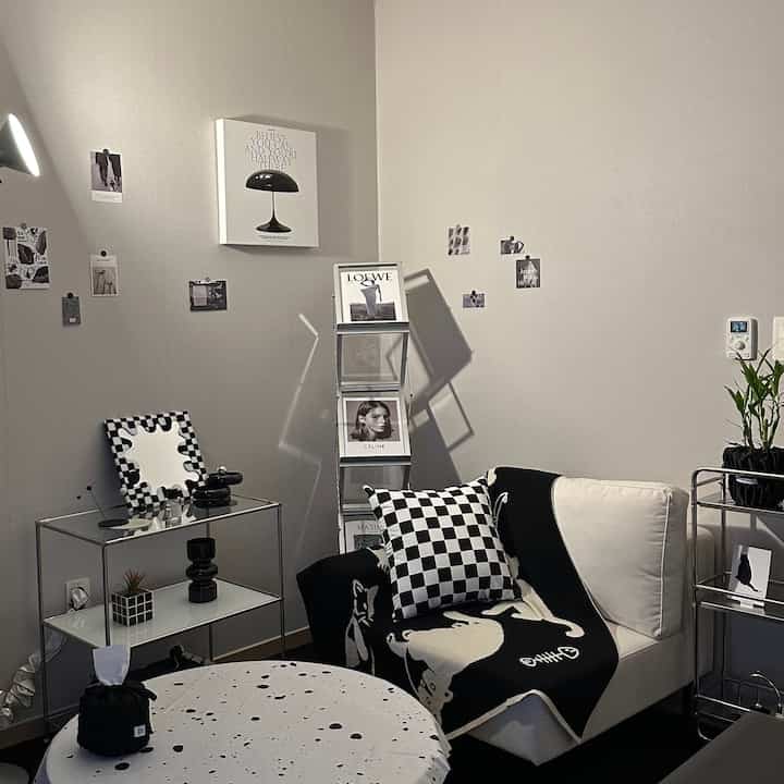 白い壁の黒白ミッドセンチュリーモダン風リビング、チェッカー柄クッションと猫柄スローがある一人掛け椅子とミニマルな収納家具の配置