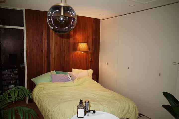 Bedroom in wood tone and white palette featuring a yellow bedspread, wall sconce, and pendant light creating a warm atmosphere