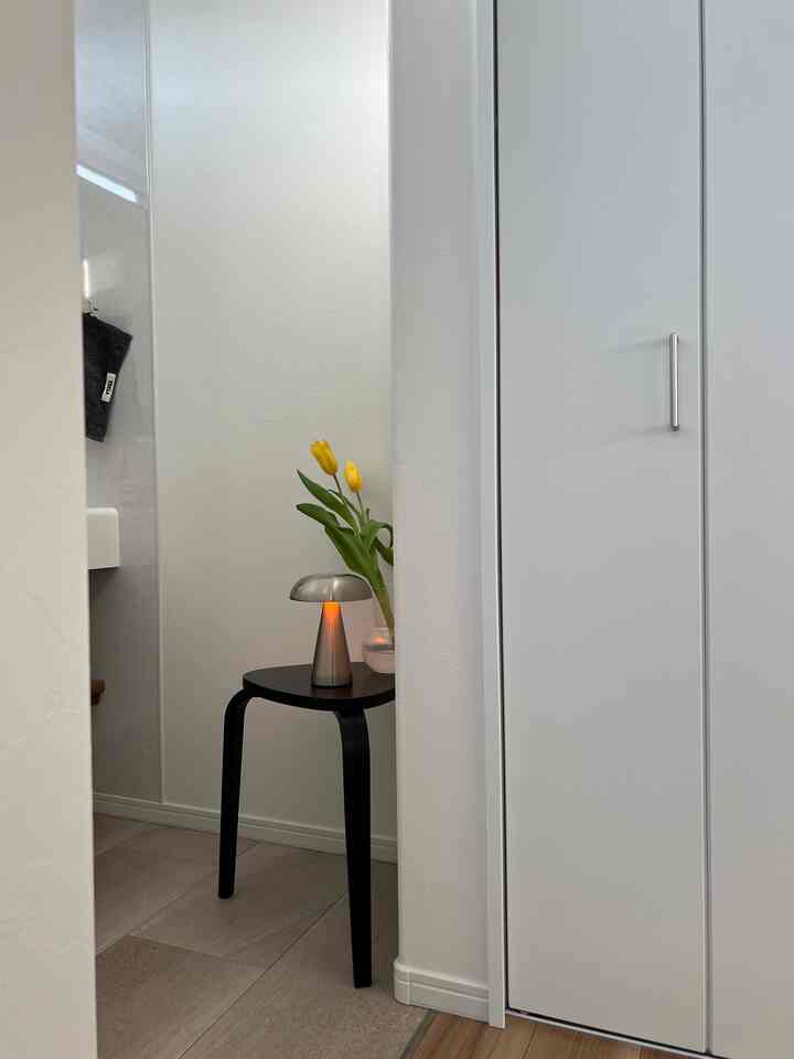 白い壁と黒いスツール、黄色のチューリップの花瓶とテーブルランプが置かれたシンプルな玄関のインテリア