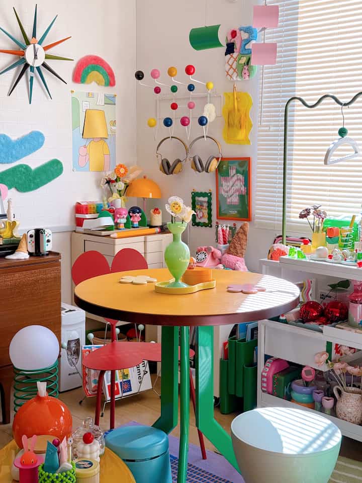 カラフルでレトロなリビングルーム、中央にオレンジの丸テーブルと緑の花瓶が配置された印象的なインテリア