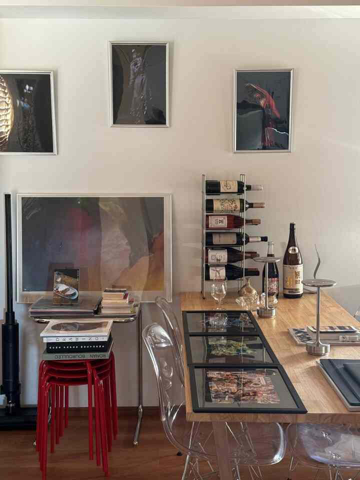 ウッドトーンの床とテーブルがある一人暮らし向けの1LDKダイニングルーム、透明な椅子と赤いスツールが配置されたすっきりとした空間