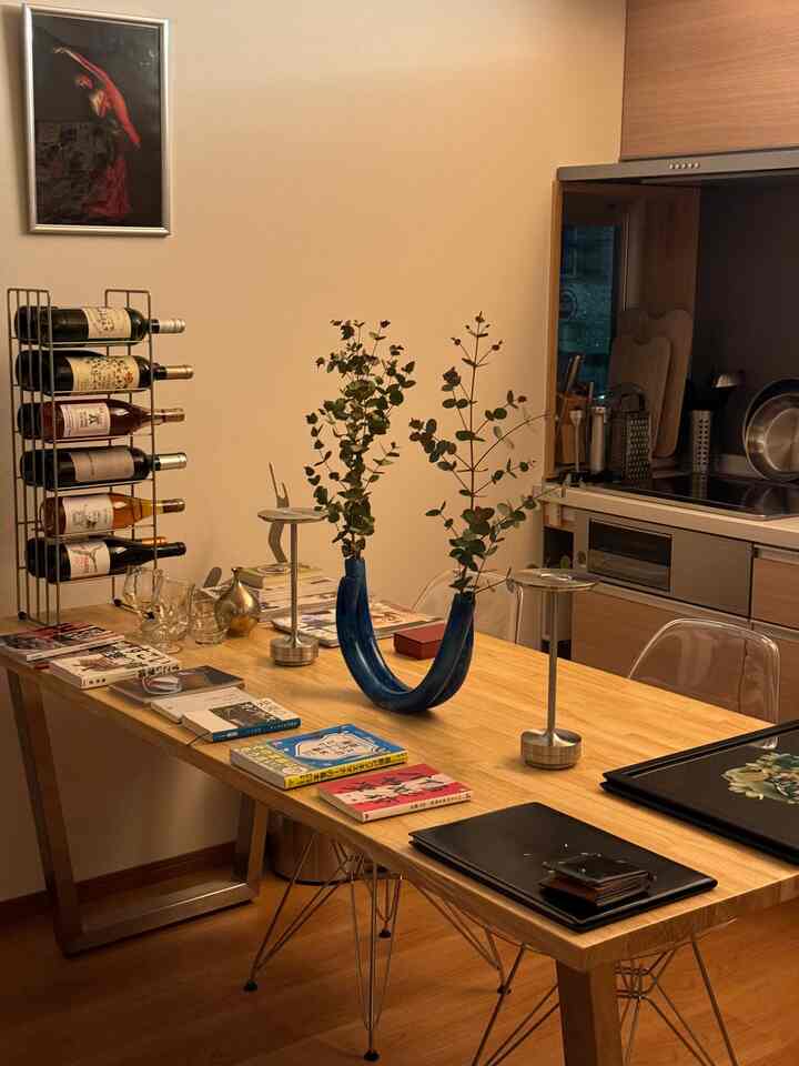 青のアクセントが効いたナチュラルウッド調の1LDKキッチンダイニング、透明な椅子とワインラックが配置された印象的な空間