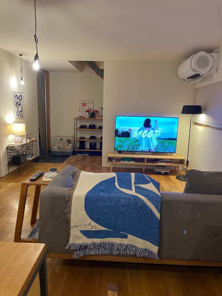 Nordic-style living room with warm wood flooring and gray sofa, featuring a blue blanket and a rabbit cage blending into the interior