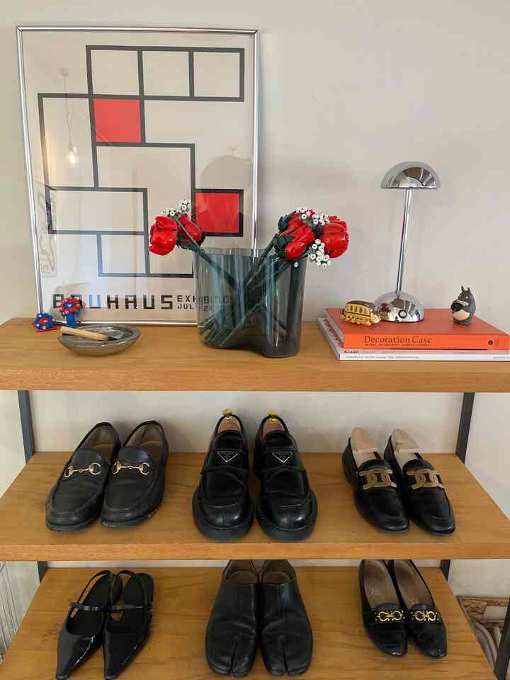 Natural toned Nordic interior space featuring a shoe cabinet with black shoes and red flower decor in a simple, orderly setting