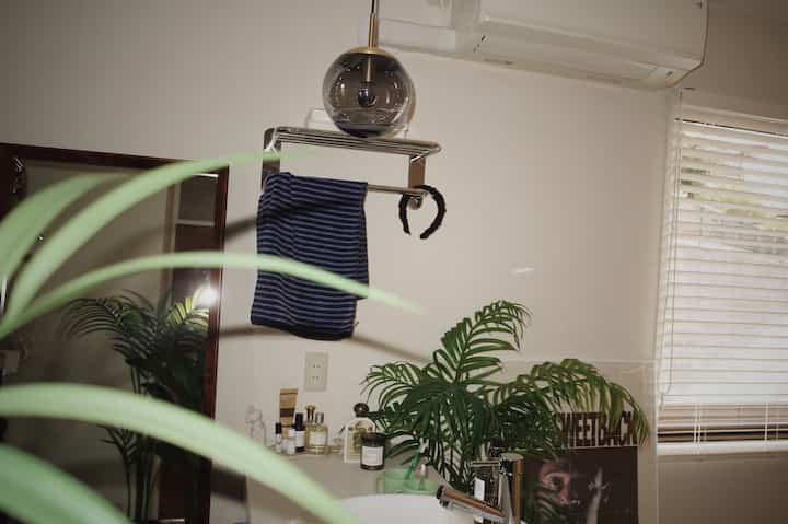 ナチュラルカラーとホワイトのバスルームには、植物とブルーストライプのタオルが配置され、落ち着いた雰囲気のインテリア