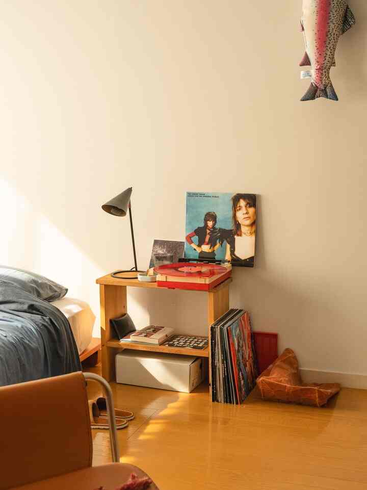 ウッドトーンと赤のアクセントがあるワンルームの寝室、ナイトテーブルの上にレトロなポータブル・レコードプレーヤーが置かれた雰囲気のあるインテリア