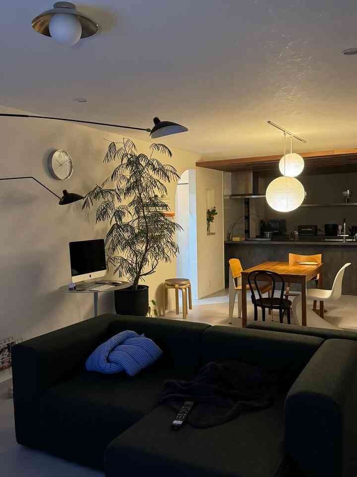 ナチュラルトーンの北欧リビング、ダークグリーンの大きなソファと丸いペンダントライトが配置された落ち着いた空間