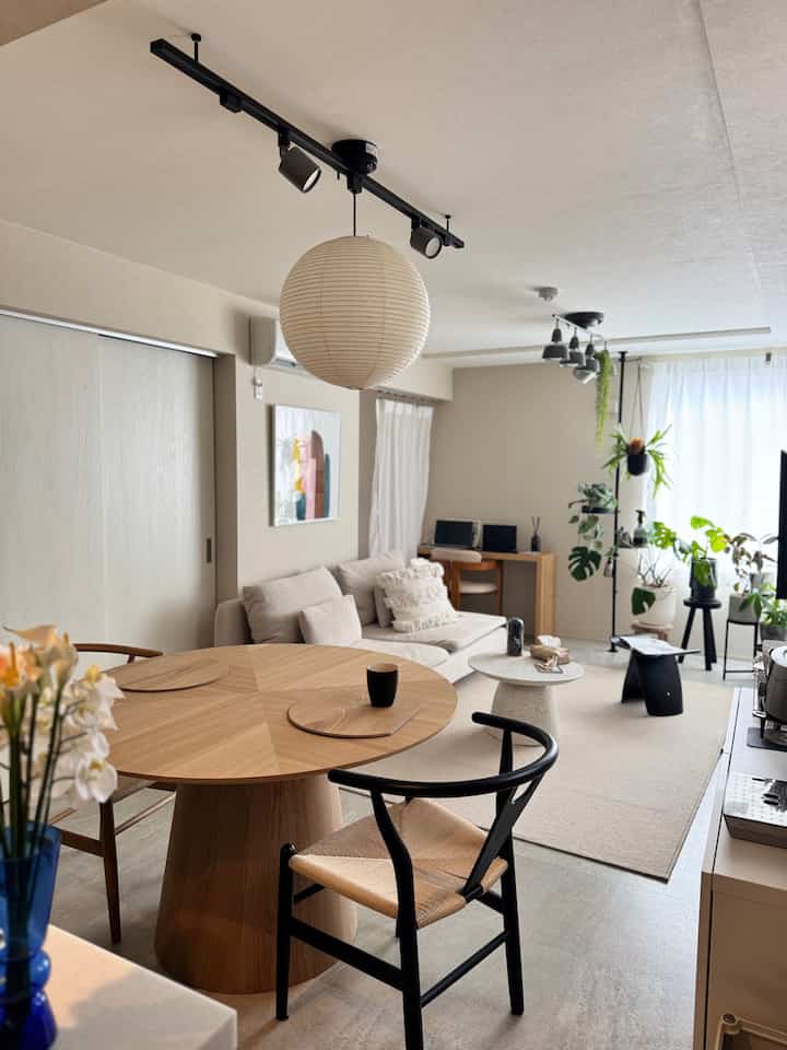 ナチュラルな色調の2LDKリビング、木製のダイニングテーブルと北欧風ソファ、多彩な植物が配置された雰囲気のある空間