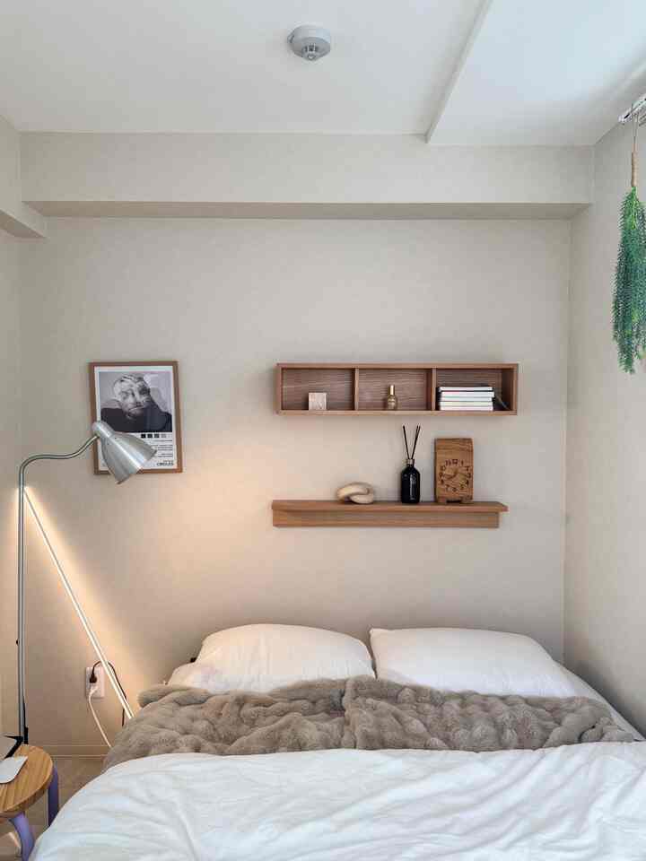 Beige-toned bedroom with wooden wall shelves, white bedding, and a floor lamp creating a natural and modern atmosphere
