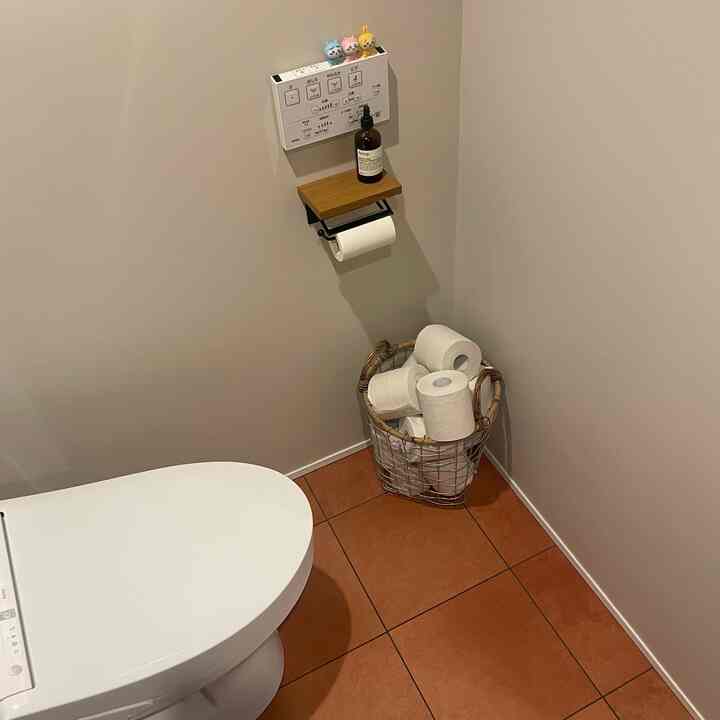 白と茶色のトーンのトイレ、きれいな便器と壁の棚、そして収納用ワイヤーバスケットがある印象的な空間