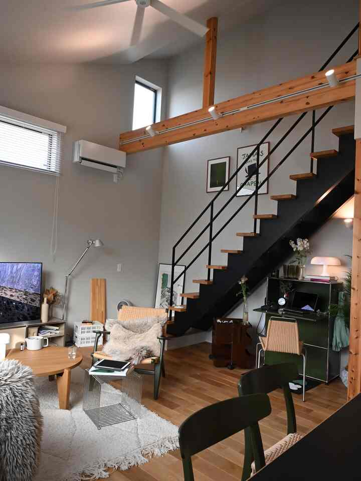 ナチュラルカラーのミッドセンチュリーモダンなリビング、木の床と階段下のデスク、アームチェアが配置された落ち着いた空間