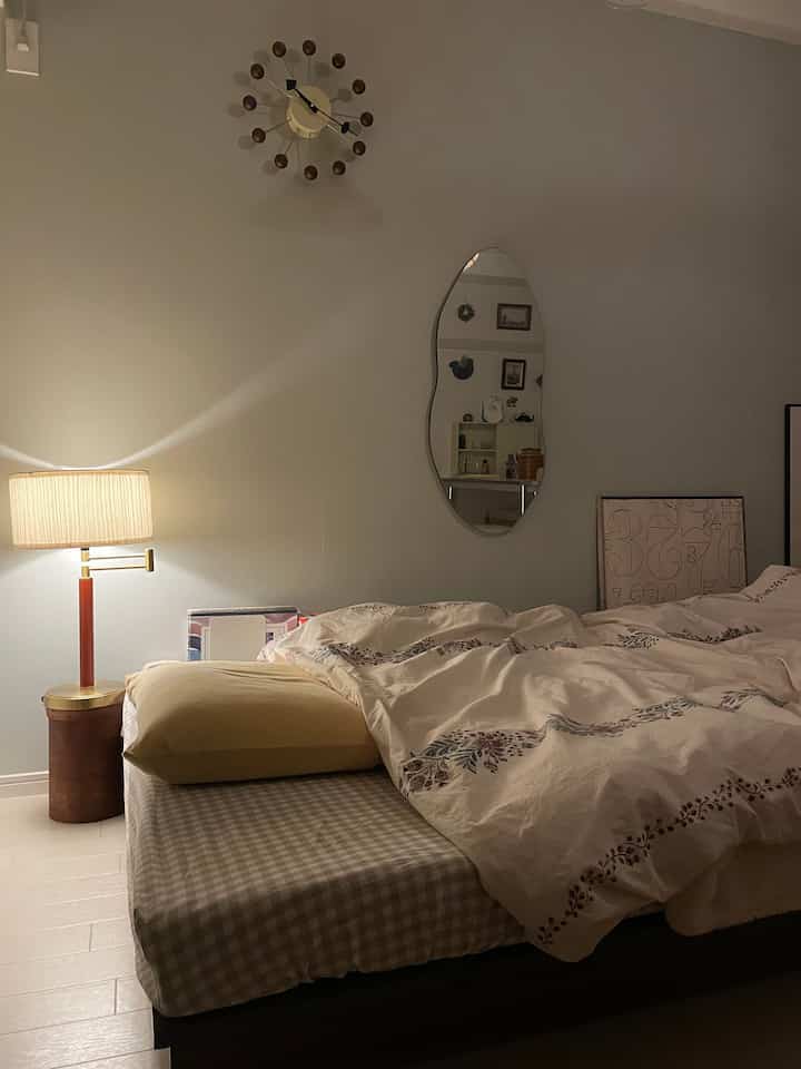 White and wood tone 8-tatami studio bedroom featuring a bed, table lamp, and an irregular wall mirror with a vintage ambiance