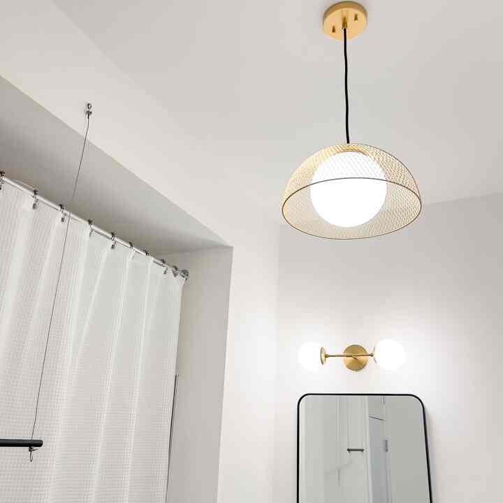White and gold toned bathroom featuring a metal mesh pendant ceiling light and wall sconces, with a clean and minimalist atmosphere