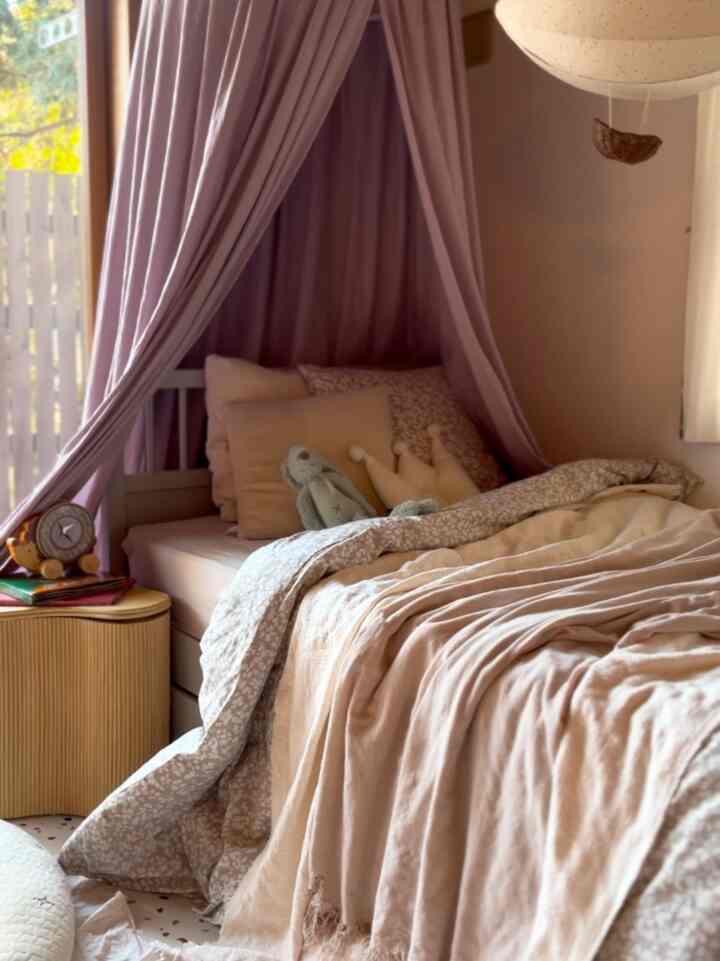 ピンクのキャノピーとベージュのブランケットがある子供部屋、柔らかく居心地の良い雰囲気のインテリア