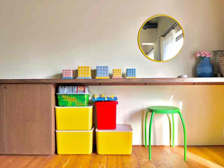 黄色と緑が特徴的なリビング、玩具収納とカウンターテーブル、黄色の鏡と花瓶が配置された雰囲気のある空間