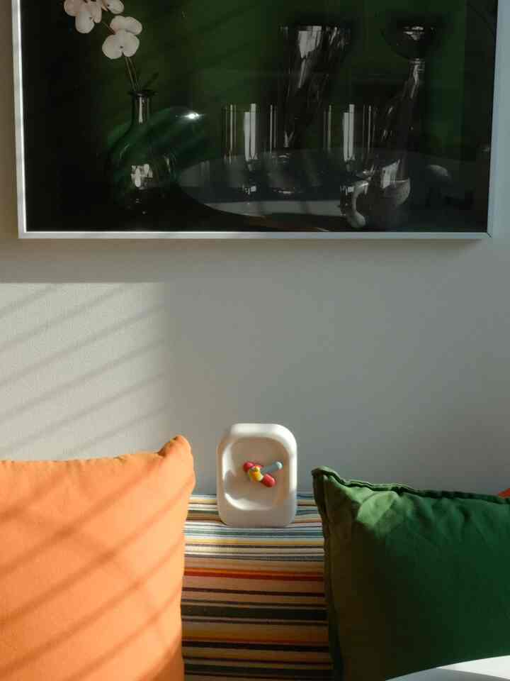 Mid-century modern studio living room with orange and green cushions on a striped throw and a minimal white clock as focal point