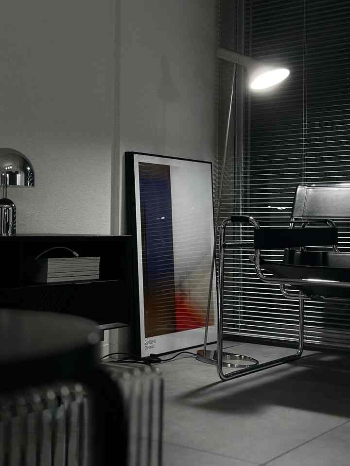 グレーと黒のトーンのリビングコーナー、黒革のアームチェアとフロアランプ、抽象的なポスターが配置されたシンプルな空間