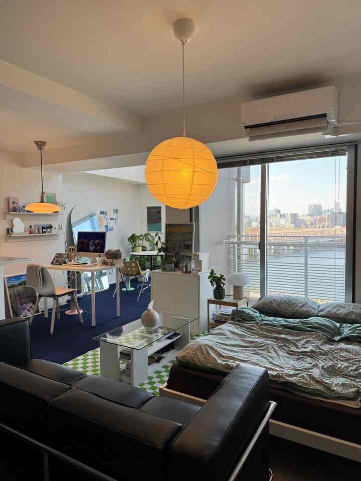 白とネイビーのトーンのワンルーム、ベッドやソファ、デスク、ペンダントライトが配置された雰囲気のあるインテリア