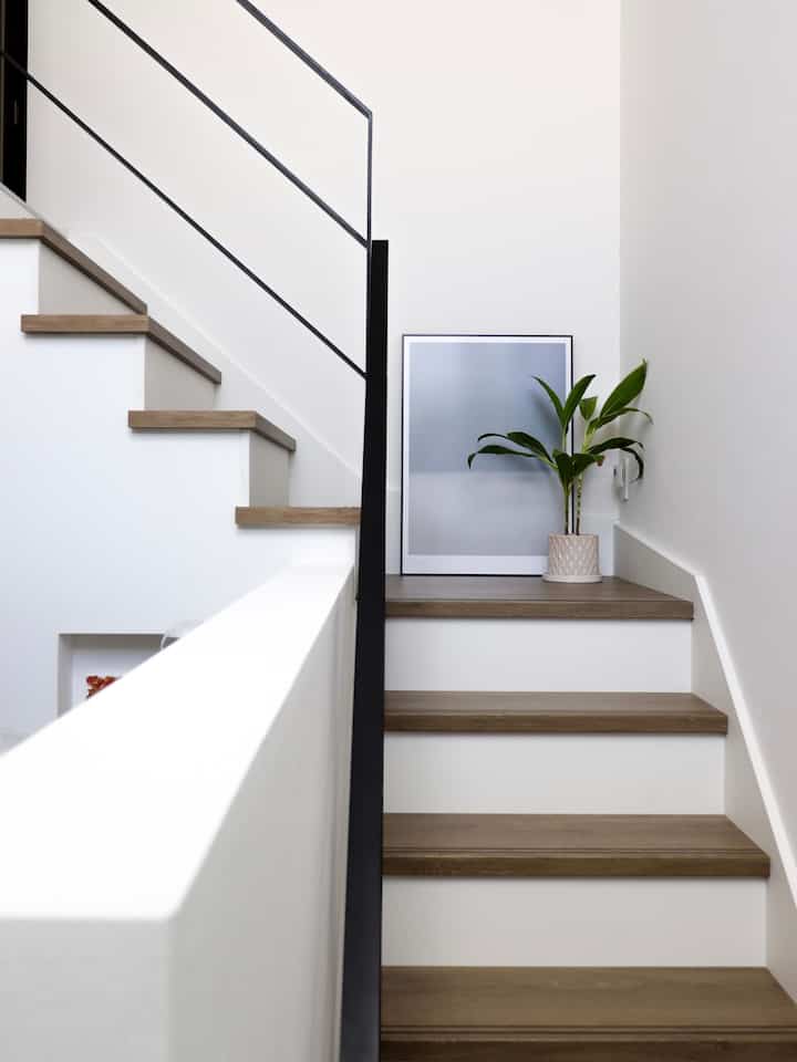 白と茶色のトーンの階段空間、ポスターと植物が配置されたシンプルでナチュラルな印象的なインテリア