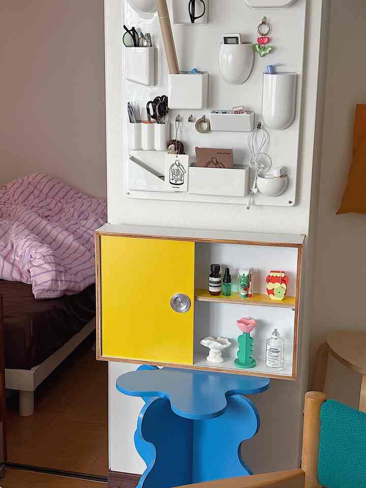 A cozy bedroom space featuring a wall-mounted storage box with a bright yellow sliding door and a blue stool underneath