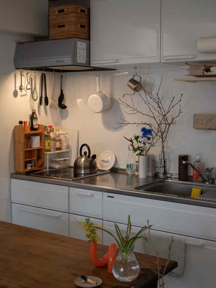 ナチュラルなトーンの一人暮らしキッチン、白い収納と木製テーブル、花瓶と調理器具が整然と配置された雰囲気のあるインテリア