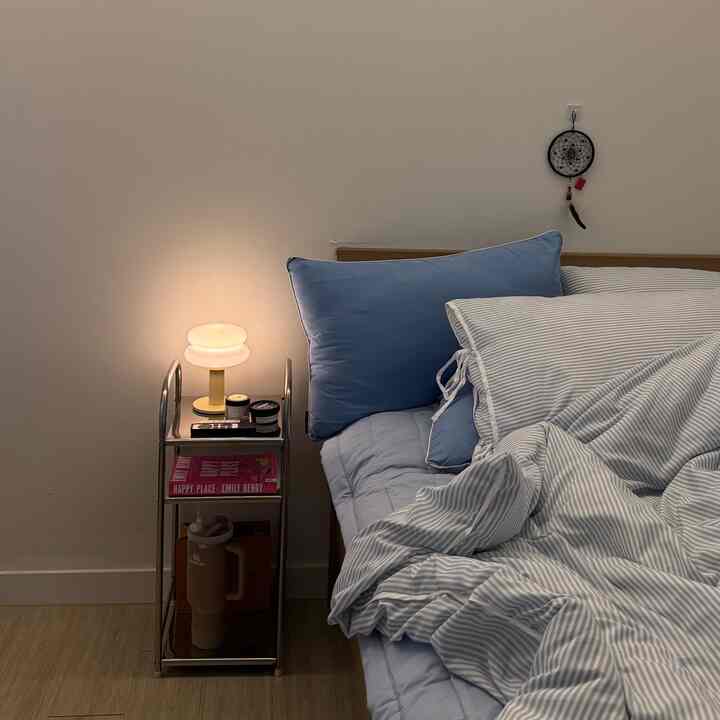 Simple bedroom featuring a nightstand with soft lighting and blue-toned bedding on the bed