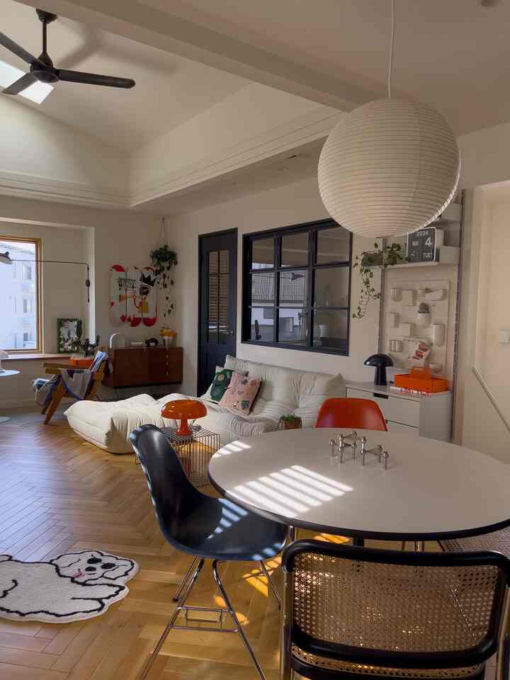 白とブラウンの木目調が調和したダイニングリビング、ミッドセンチュリーモダンなラウンドテーブルとソファが配置されたナチュラルな空間