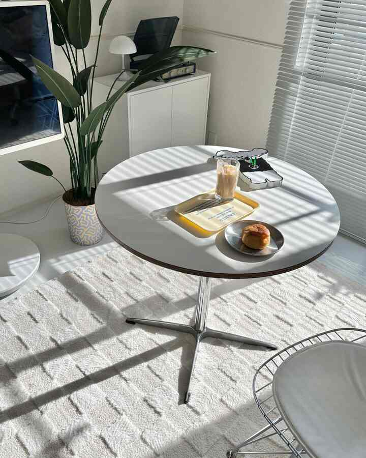 Bright white and green toned studio apartment cafe-style space featuring a round table, a plant, and a comfortable chair for a cozy home cafe vibe