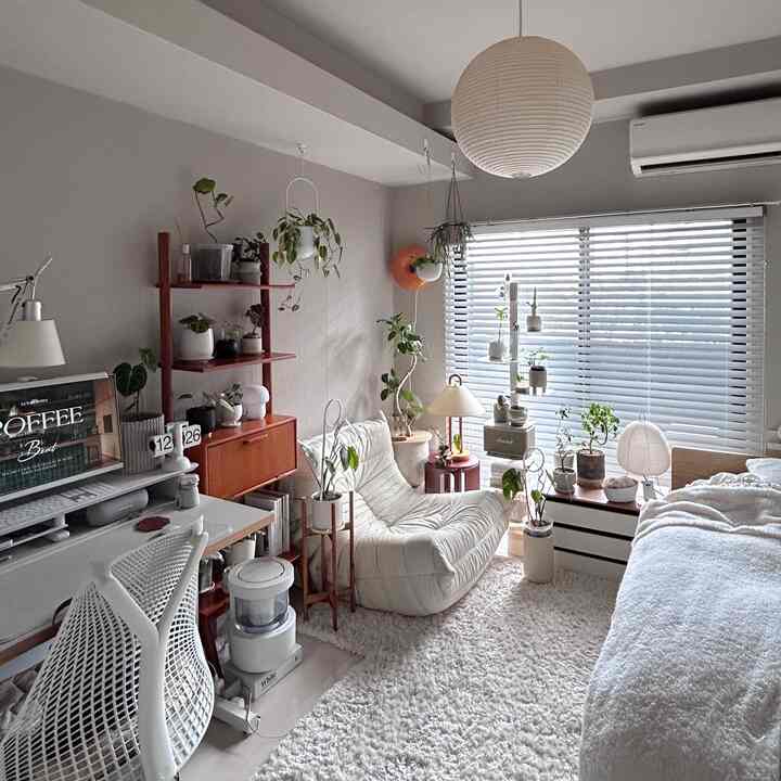 White-toned 1K bedroom and home office featuring numerous plants and a cozy lounge chair with a warm atmosphere