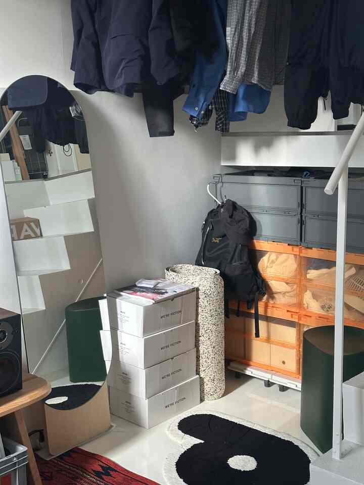 Light gray walled corner space under stairs featuring stacked storage containers and large standing mirror in a small area