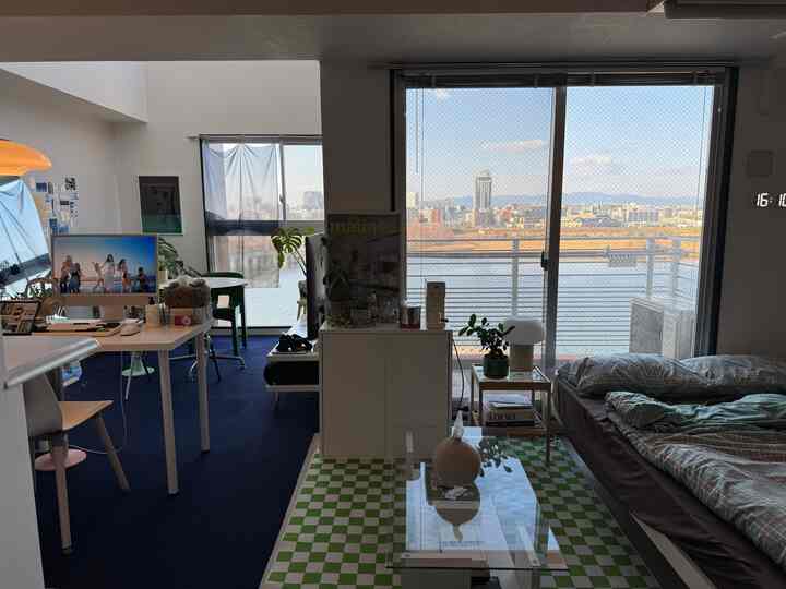 Studio apartment bedroom and home office with blue and green checkered carpets, large windows bringing bright natural light