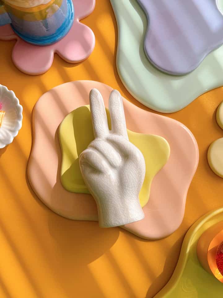 黄色い背景に白い陶器のオブジェとカラフルなパステルトレーが配置された雰囲気のあるテーブルインテリア