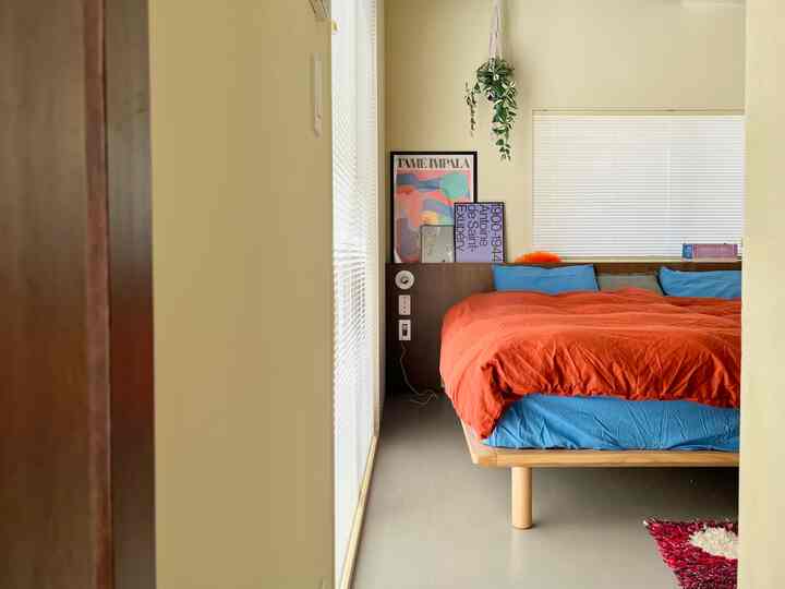 Bright wood tones and white walls in bedroom featuring an orange duvet cover as color accent