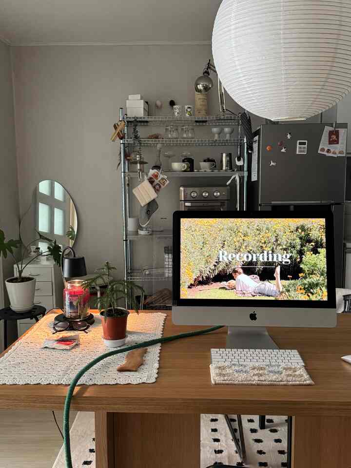A simple modern home office space featuring a white wall and wood-toned desk, with shelves and plants creating a cozy atmosphere