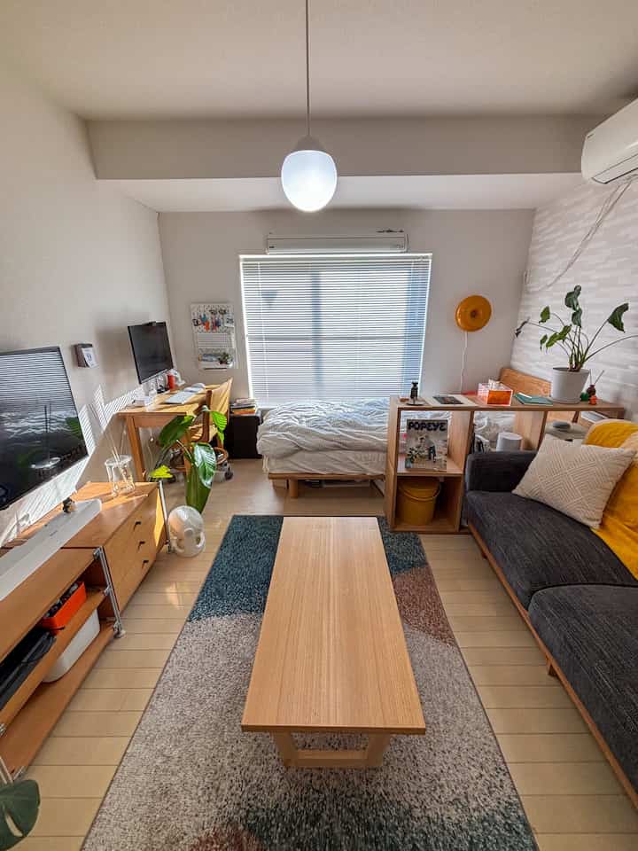 ナチュラルな木目調家具とラグが配置された1Kのワンルーム、リビングと寝室が一体となった居心地の良い空間