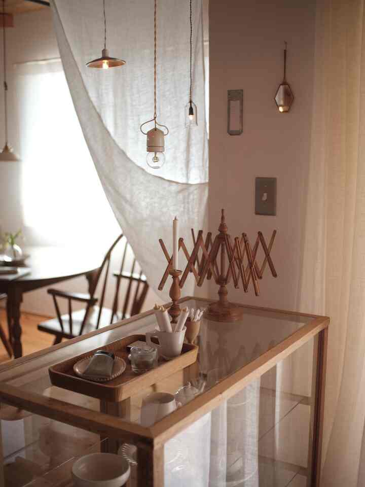 A natural wood-tone living room with transparent glass cabinet, warm beige curtains, and Art Deco style lighting creating a cozy atmosphere