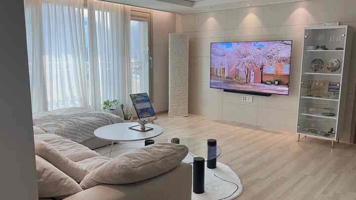 明るいホワイトとウッドトーンのリビング、ベージュのソファと丸いホワイトテーブル、壁掛けテレビがあるシンプルモダンな空間