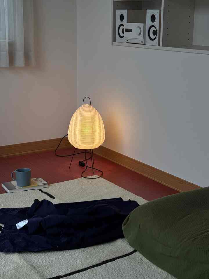 白い壁と赤いタイル床のリビング、アカリランプと緑のビーズクッション、白いラグが配置された雰囲気のある空間