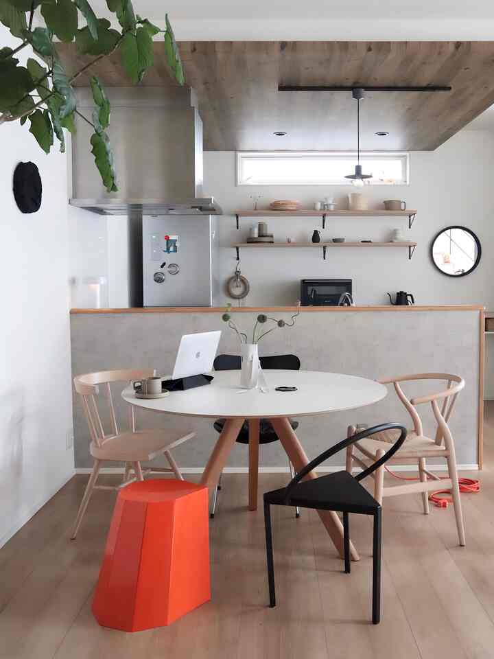 Modern minimalist dining room with white walls and brown wooden ceiling, featuring a round dining table, chairs, and an orange stool accent