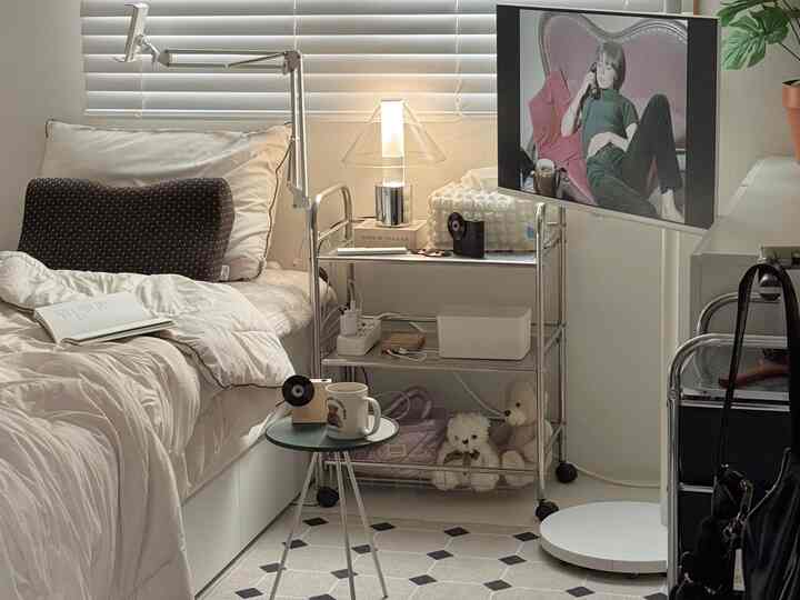 白とシルバーのトーンのワンルーム寝室、ベッドとメタル収納トロリーが配置された清潔感あるナチュラルモダンなインテリア