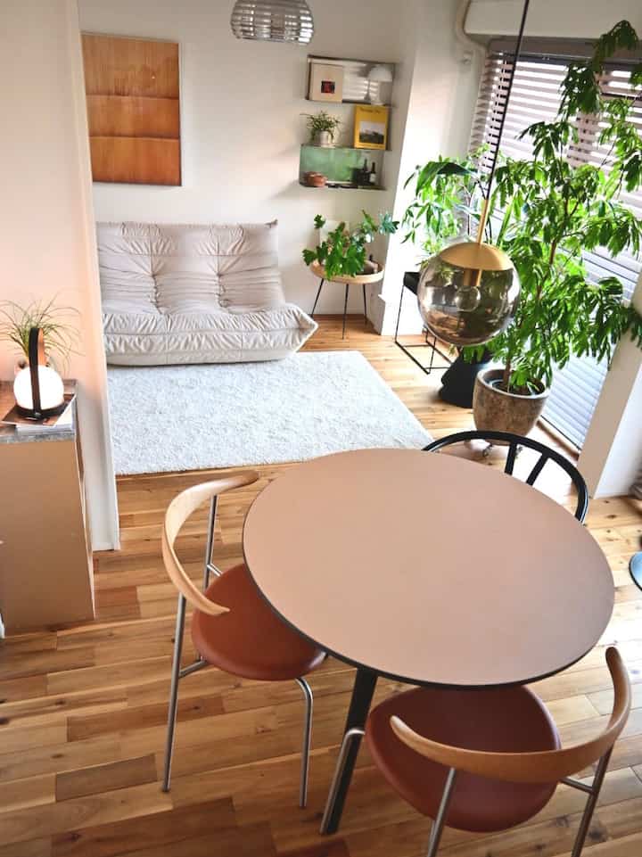 Bright beige and wood-toned living and dining room featuring a round dining table with brown chairs and green plants, creating a natural atmosphere