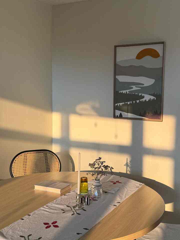 Warm natural-toned dining room featuring a wooden dining table and chair, wall art, and a candle creating a cozy atmosphere