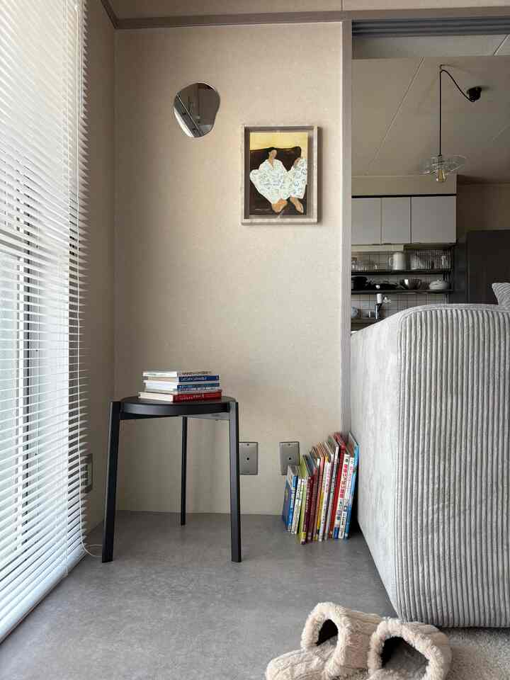 ベージュとアイボリー調のリビング、コーナーに整理された本と黒いスツールが配置された、シンプルで自然なモダンな空間