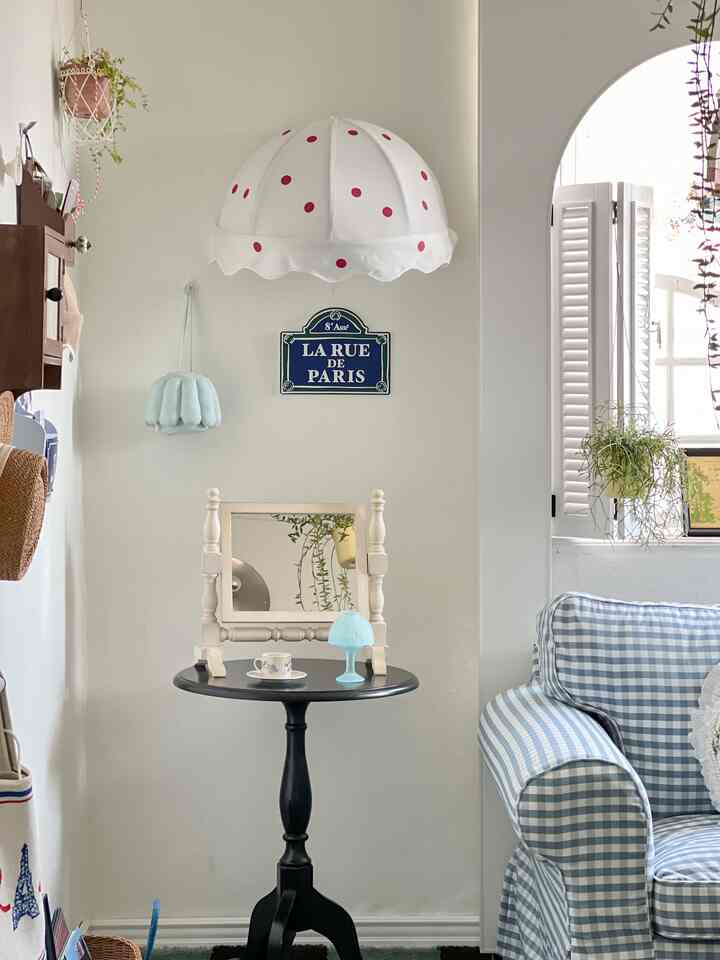 白い壁に黒のサイドテーブルを配したフレンチカントリー風リビング、青いチェック柄のソファとかわいいインテリアが配置された空間