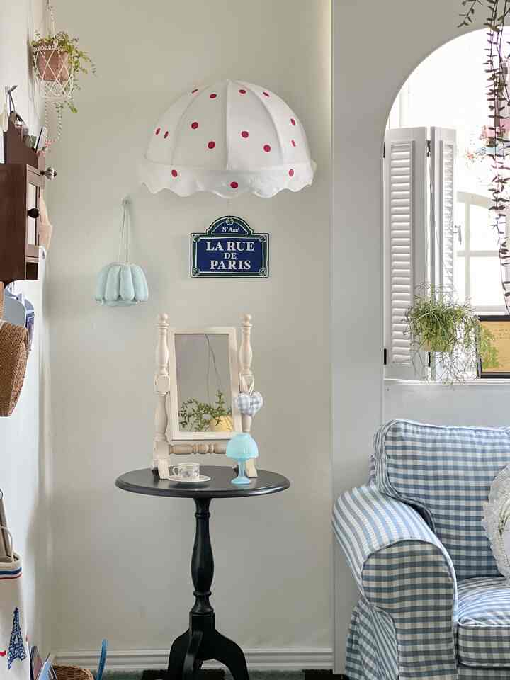 白と青のトーンのリビング、ギンガムチェックのソファと黒の丸いサイドテーブル、フレンチスタイルの小物が配置された雰囲気のあるインテリア