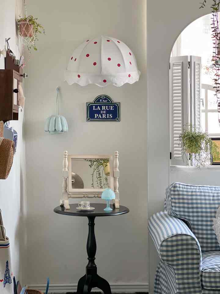 白と青の色調のリビング、ギンガムチェックのソファと黒のサイドテーブルにテーブルランプとティーカップが置かれた雰囲気のあるフレンチカントリースタイルのインテリア