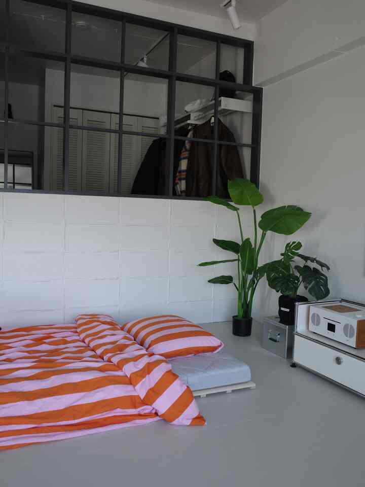 ホワイトトーンの狭い一人暮らし用寝室、床にオレンジのストライプ寝具が置かれた自然な雰囲気のインテリア